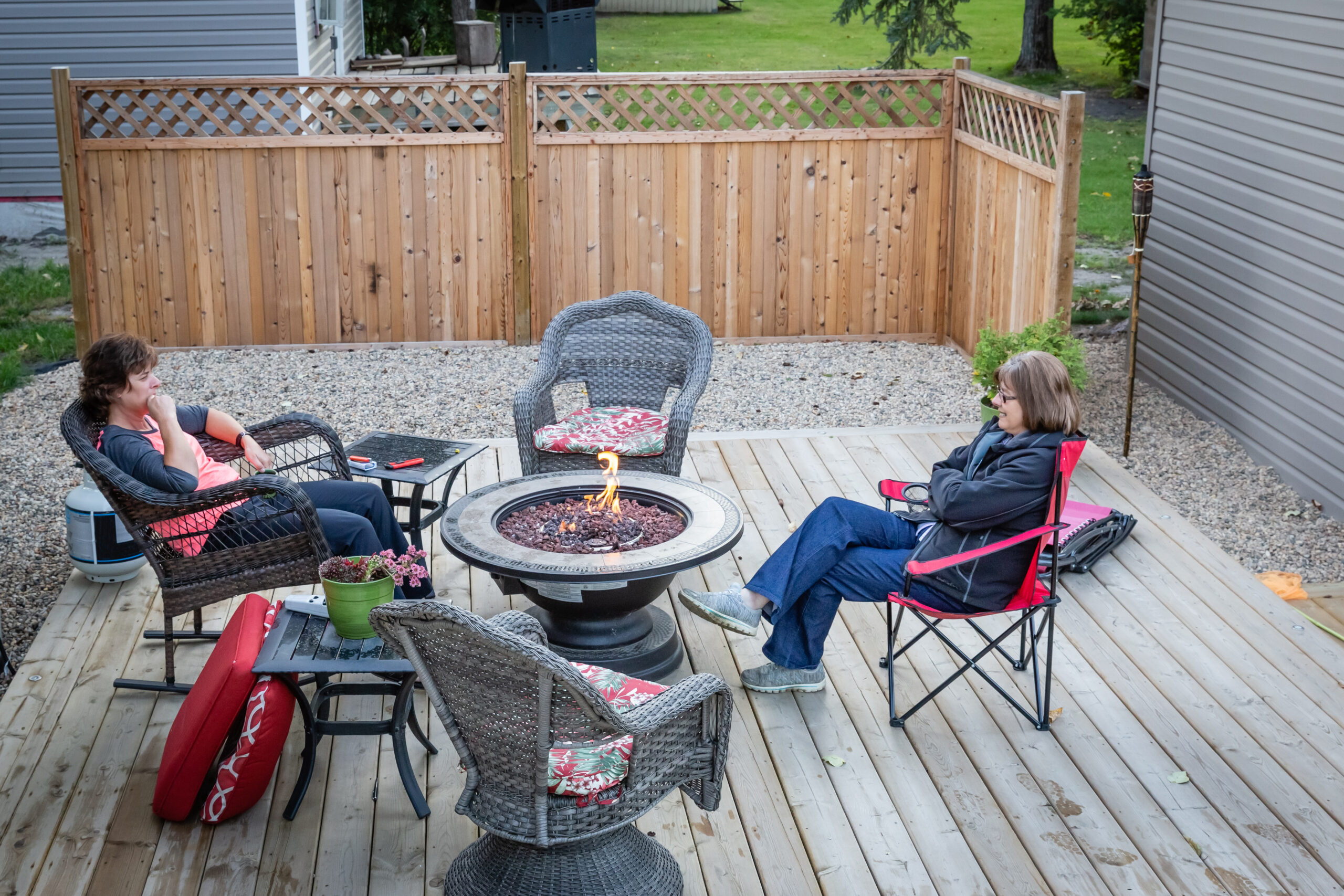 Palenisko na tarasie z desek. Dookoła paleniska na krzesłach siedzą osoby.