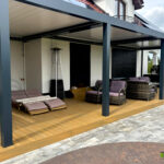 Szeroki, rozbudowany taras z deski kompozytowej, umieszczony przy domu wraz z zadaszeniem i umeblowaniem. Taras zrealizowany przez Fabrykę Tarasów.